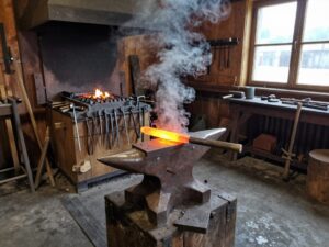 Traditionelle Schmiede mit Amboss, Hammer und glühendem Stahl auf der Werkbank, dampfende Hitze im Hintergrund