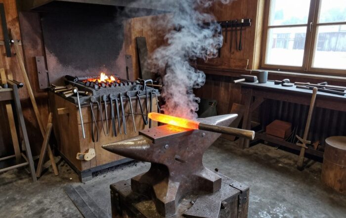 Traditionelle Schmiede mit Amboss, Hammer und glühendem Stahl auf der Werkbank, dampfende Hitze im Hintergrund