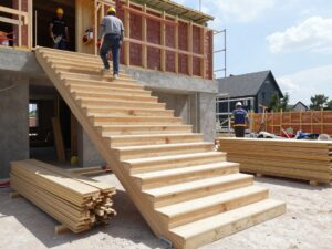 Moderne Holztreppe in Bauphase: Arbeiter mit Helmen nutzen Handwerkzeuge, Holzbretter ordentlich gestapelt neben Gerüst