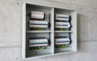 Geöffnete elektrische Unterverteilung mit ordentlich verlegten Leitungssperren und Sicherungsautomaten an einer Betonwand.